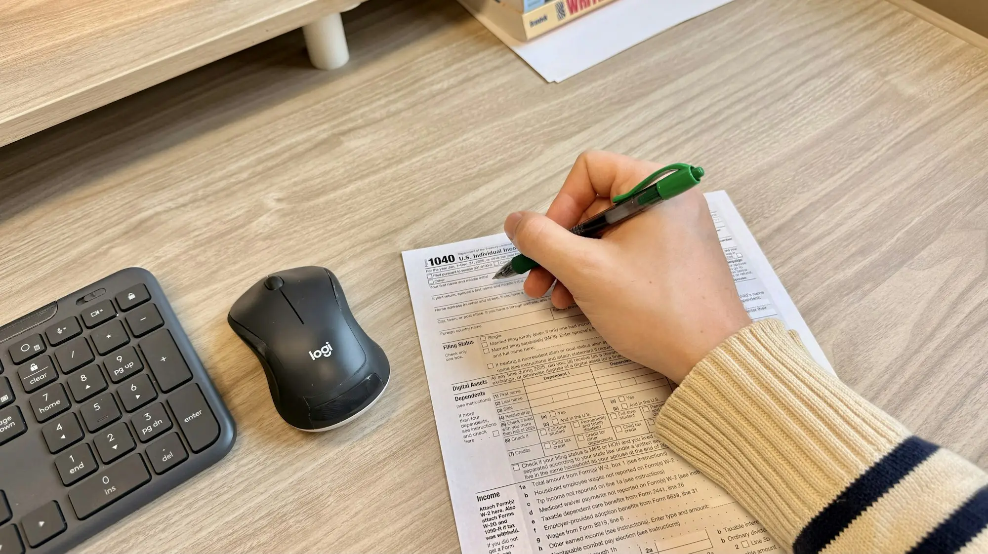 Hand signing a finance document next to a keyboard and mouse